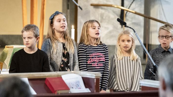 Några barn står bredvid varandra och sjunger framme i kyrkan.