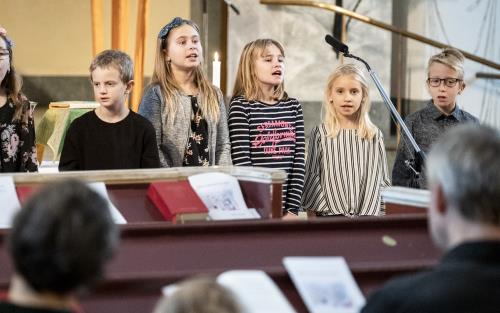 Några barn står bredvid varandra och sjunger framme i kyrkan.