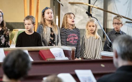 Några barn står bredvid varandra och sjunger framme i kyrkan.