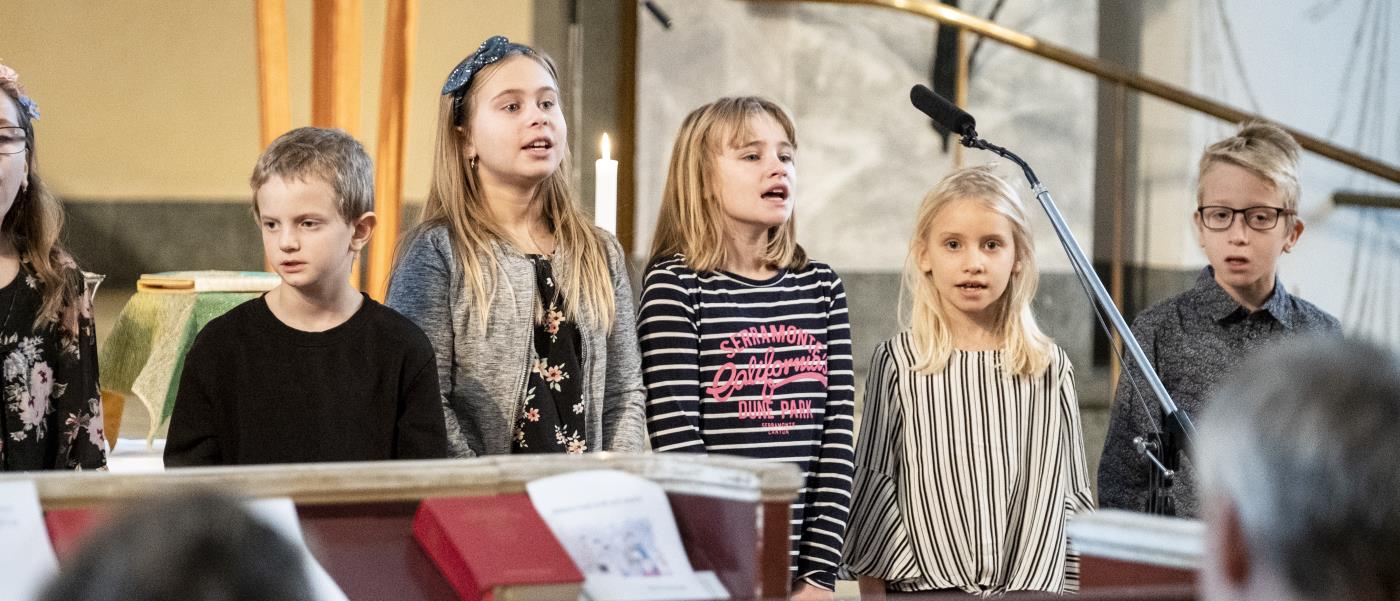 Några barn står bredvid varandra och sjunger framme i kyrkan.
