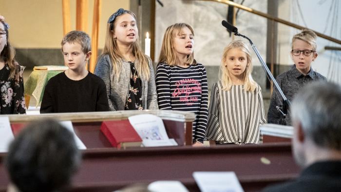 Några barn står bredvid varandra och sjunger framme i kyrkan.