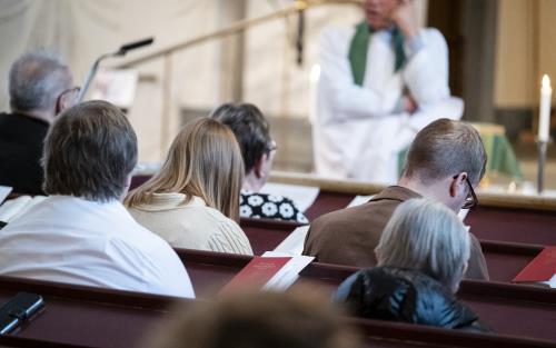 En församling sitter i kyrkans bänkrader.