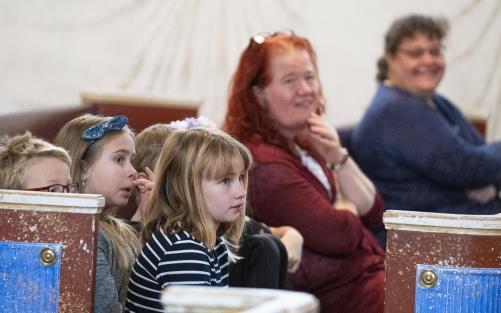 Några barn och vuxna i kyrkbänken lyssnar till prästen.