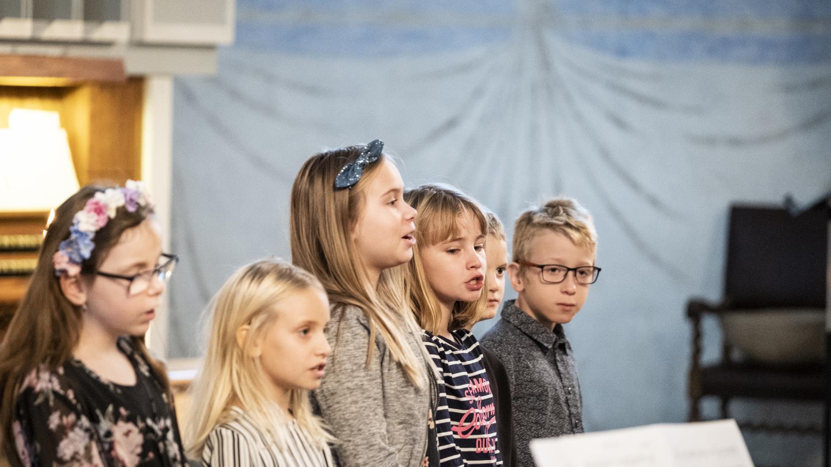 Några barn står bredvid varandra och sjunger framme i kyrkan.