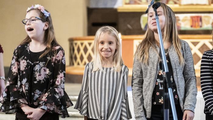 Några flickor står bredvid varandra framme i koret i en kyrka och sjunger glatt.