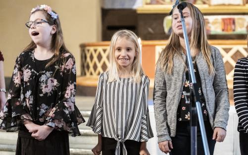 Några flickor står bredvid varandra framme i koret i en kyrka och sjunger glatt.