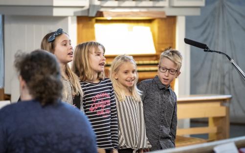 Några barn sjunger framför en mikrofon i en kyrka.