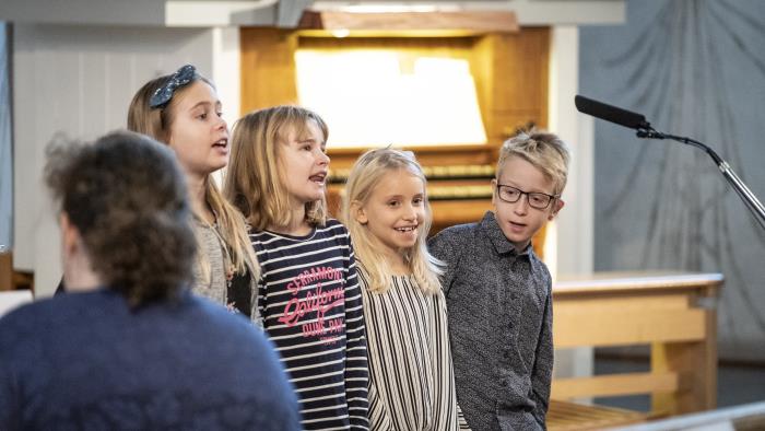 Några barn sjunger framför en mikrofon i en kyrka.