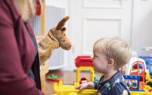 Ett barn tittar fascinerat på en handdocka som föreställer en älg.