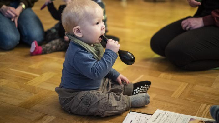 Några mammor sitter i en ring på golvet med sina bebisar. En bebis har en maracas i munnen.