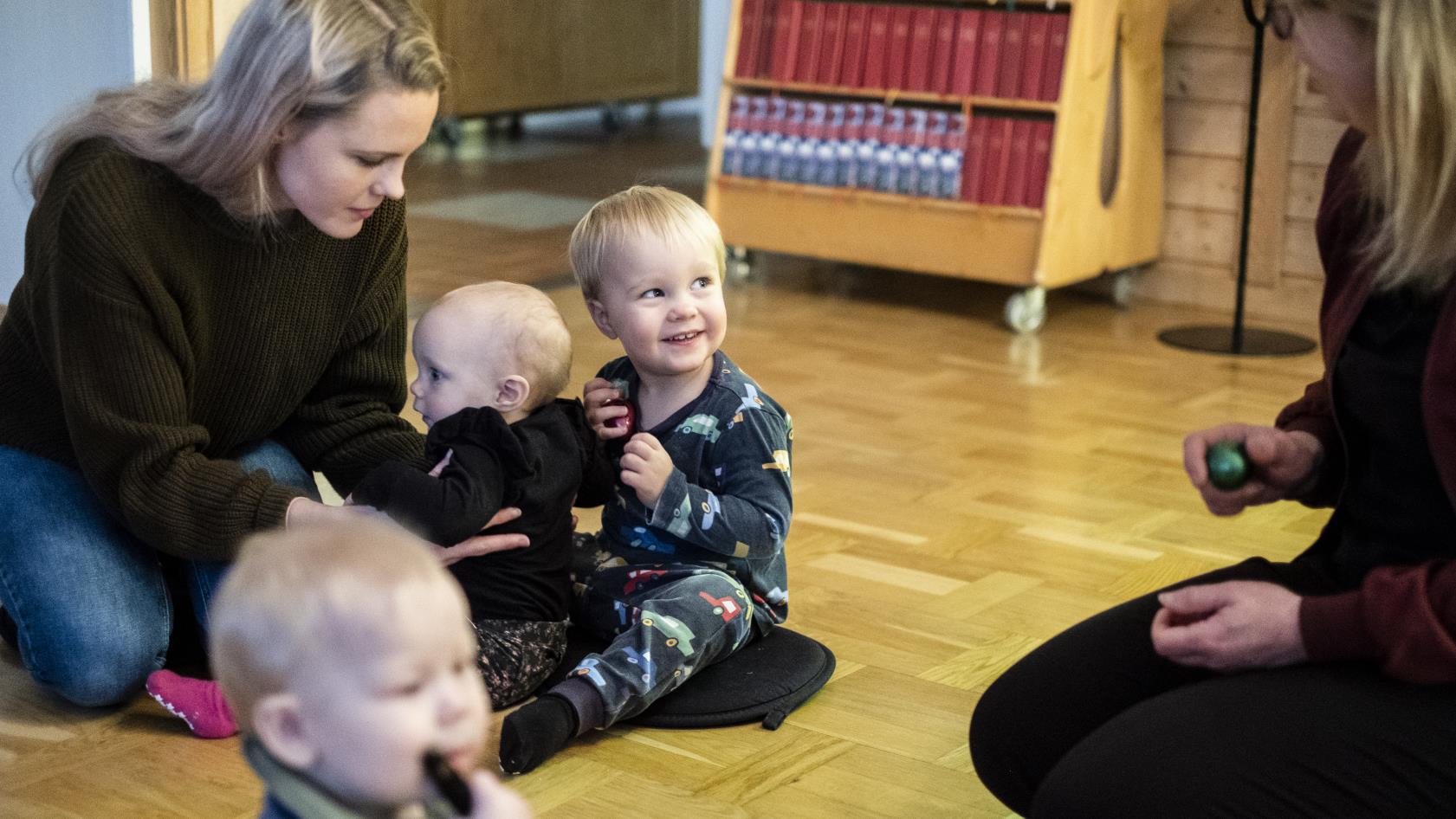 Några mammor sitter på golvet med sina bebisar.