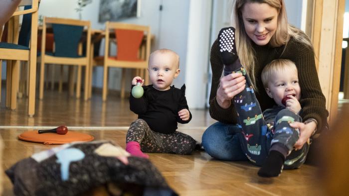 Några mammor sitter på golvet med sina bebisar.