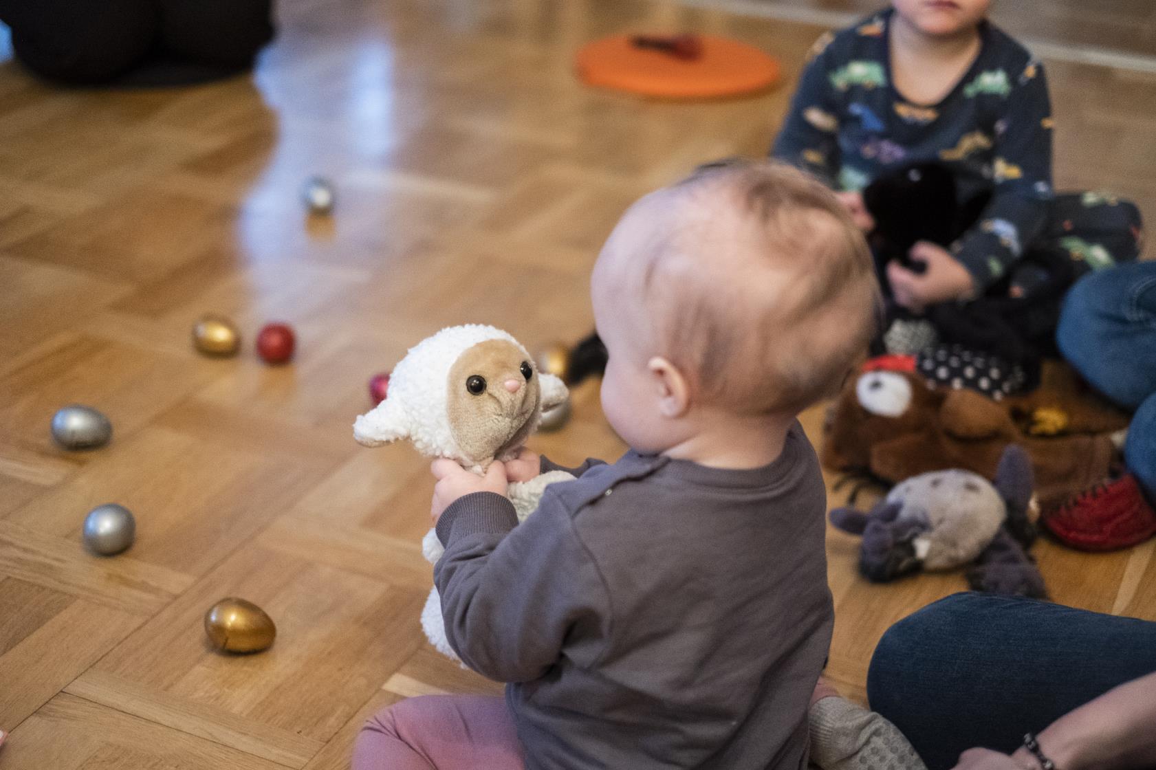 En bebis på golvet tittar på ett gosedjur som föreställer ett får.