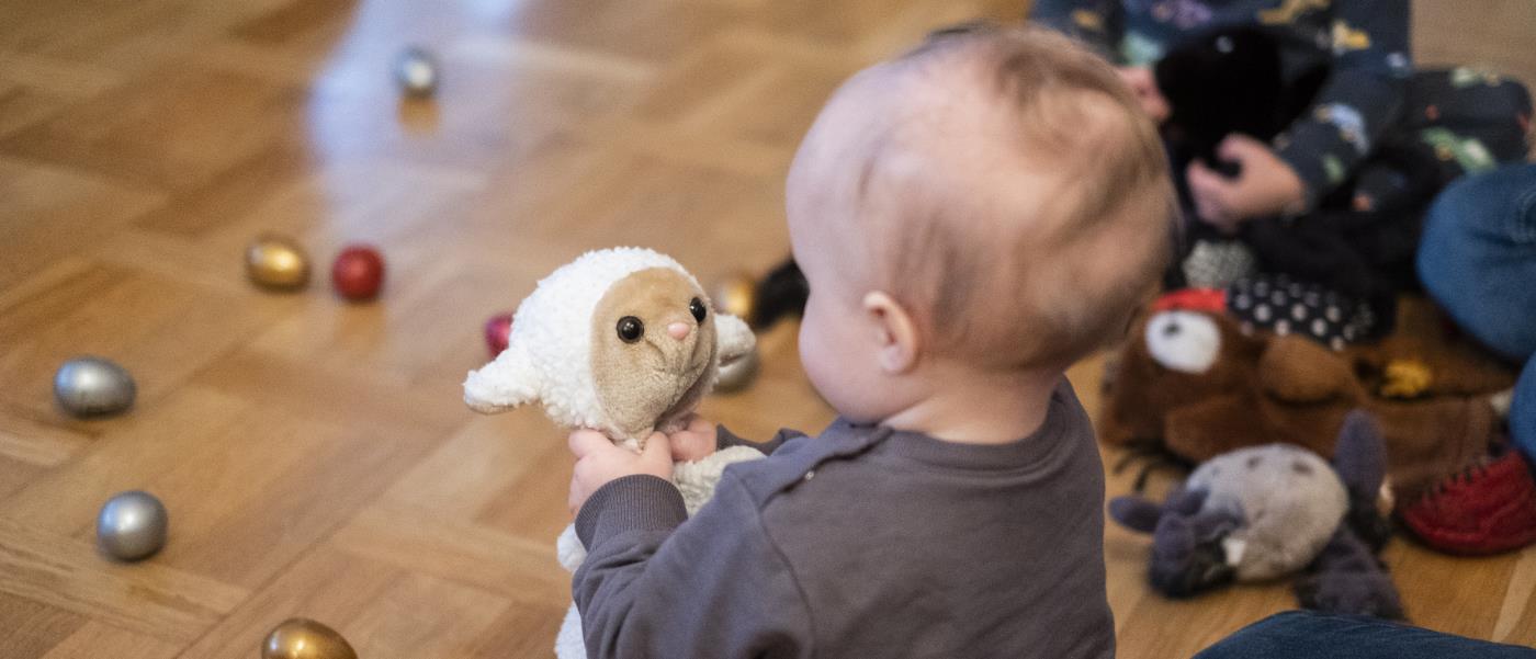 En bebis på golvet tittar på ett gosedjur som föreställer ett får.