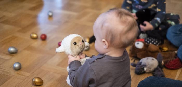 En bebis på golvet tittar på ett gosedjur som föreställer ett får.