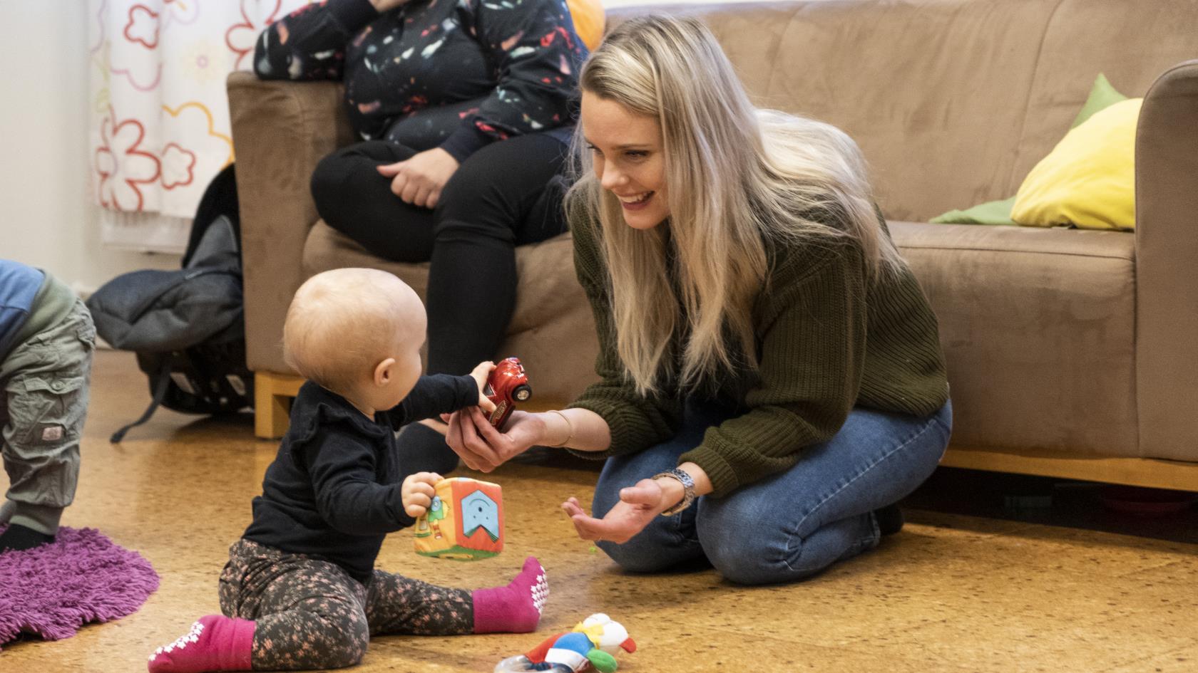 En mamma sitter på golvet och leker med sin bebis.