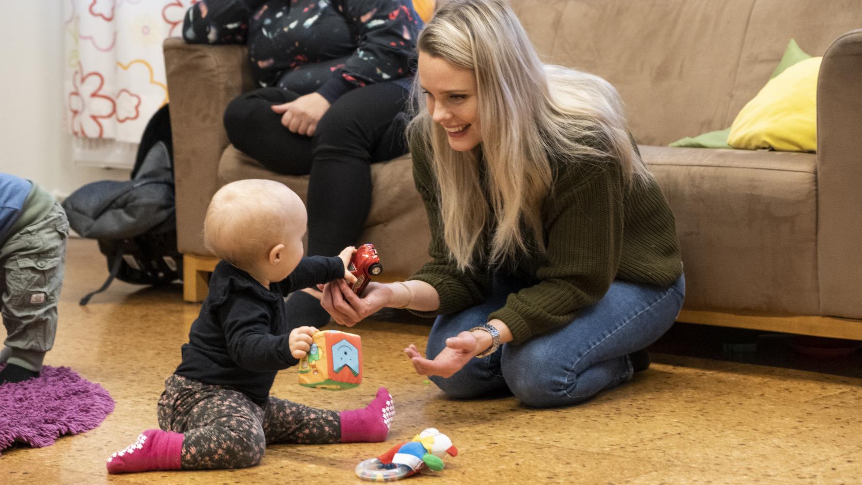 En mamma sitter på golvet och leker med sin bebis.