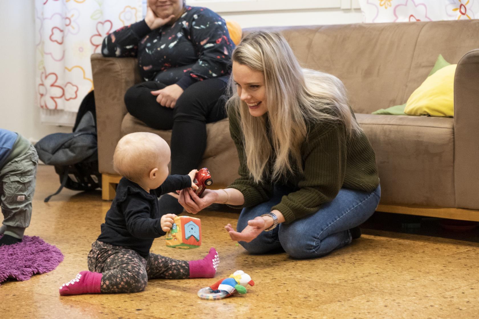 En mamma sitter på golvet och leker med sin bebis.