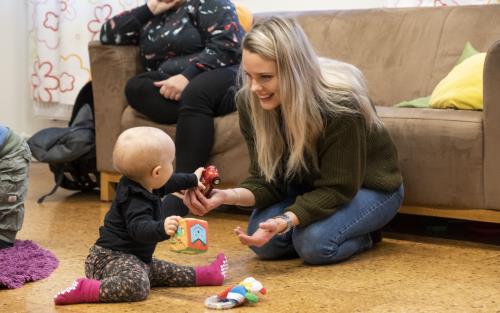 En mamma sitter på golvet och leker med sin bebis.