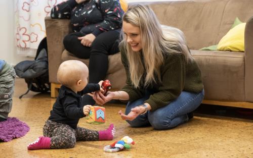 En mamma sitter på golvet och leker med sin bebis.