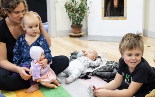 En mamma och några barn i olika åldrar sitter på golvet.