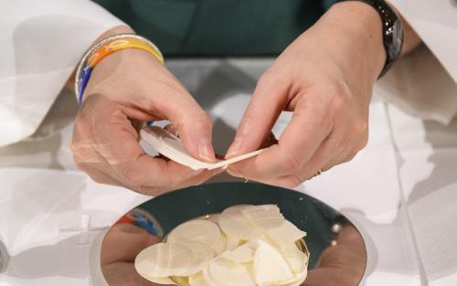 En diakon bryter isär oblater och lägger på ett fat inför nattvarden.