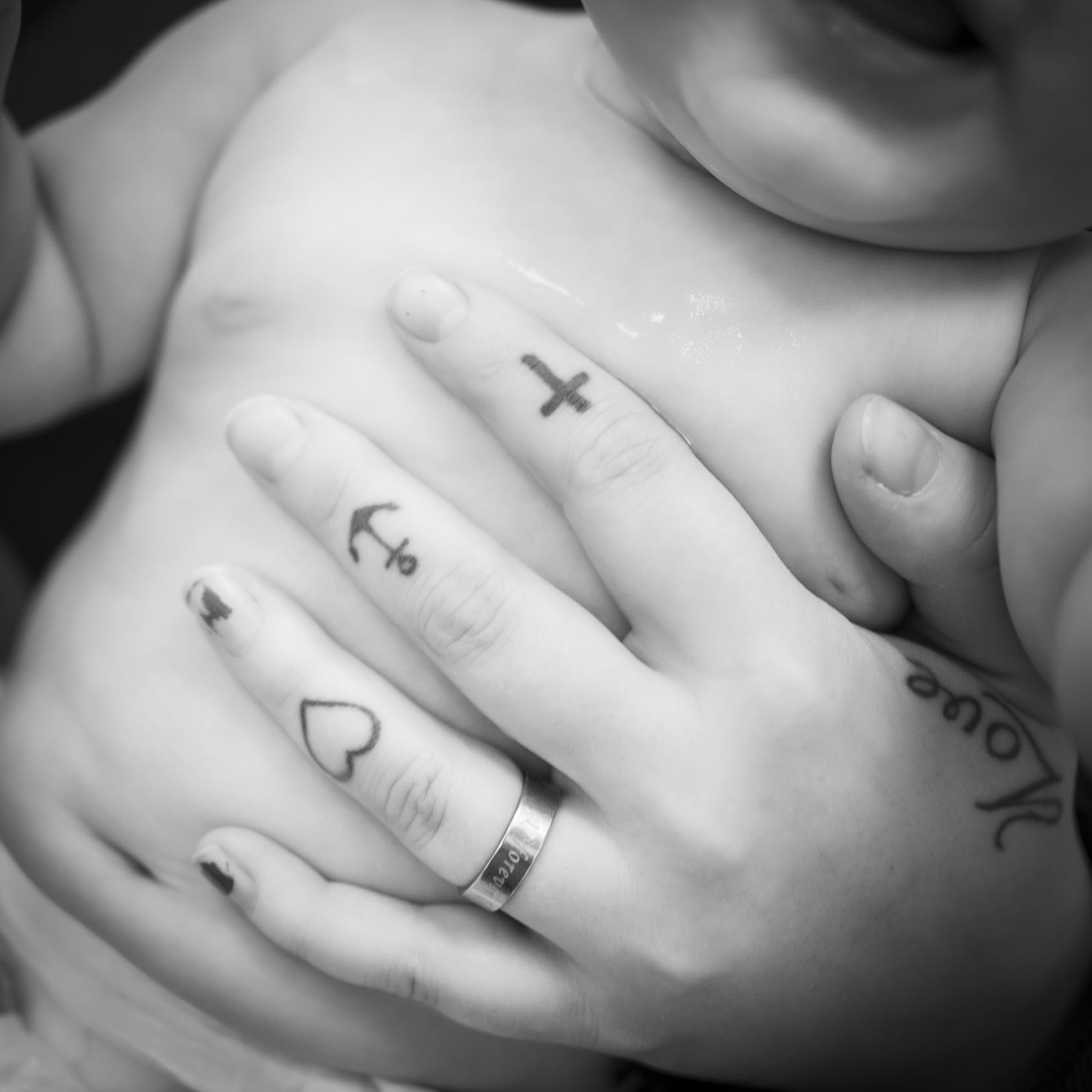 Någon med flera små tatueringar på fingrarna håller handen runt magen på en bebis.