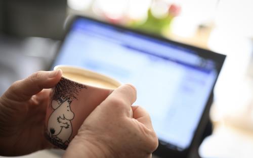 Någon sitter vid datorn och håller en kaffekopp med Mumin-motiv.