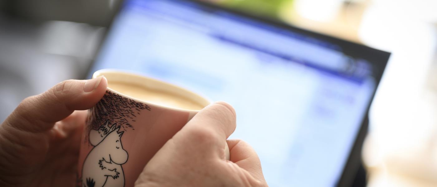 Någon sitter vid datorn och håller en kaffekopp med Mumin-motiv.