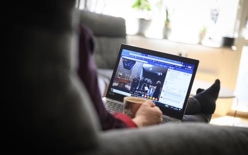 En person sitter i en soffa med sin dator i knät och följer en digital gudstjänst.