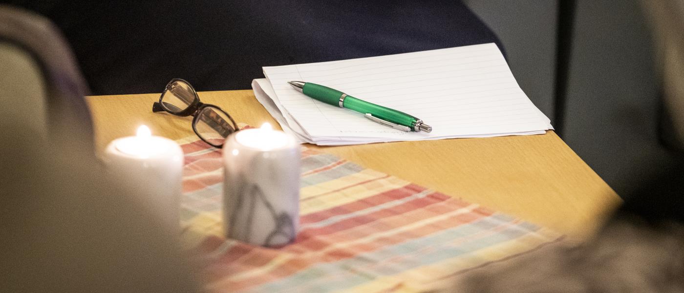 Ett par glasögon, papper och penna ligger på bordet bredvid några stearinljus.