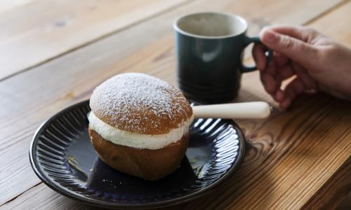 Någon sitter vid ett bord med en semla och dricker kaffe.