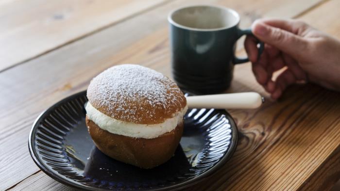 Någon sitter vid ett bord med en semla och dricker kaffe.
