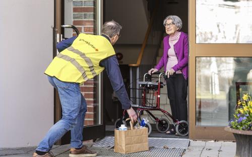 En man från Svenska kyrkan lämnar en matkasse till en äldre dam vid ytterdörren.