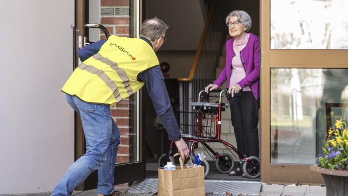 En man från Svenska kyrkan lämnar en matkasse till en äldre dam vid ytterdörren.