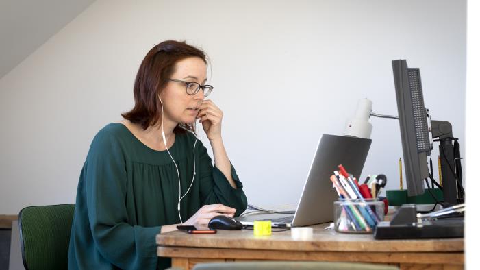 En kvinna sitter med datorn vid skrivbordet och pratar i mobiltelefon.