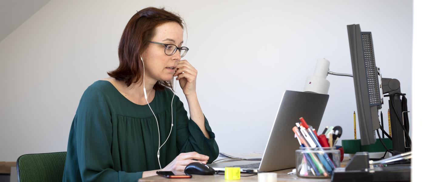 En kvinna sitter med datorn vid skrivbordet och pratar i mobiltelefon.