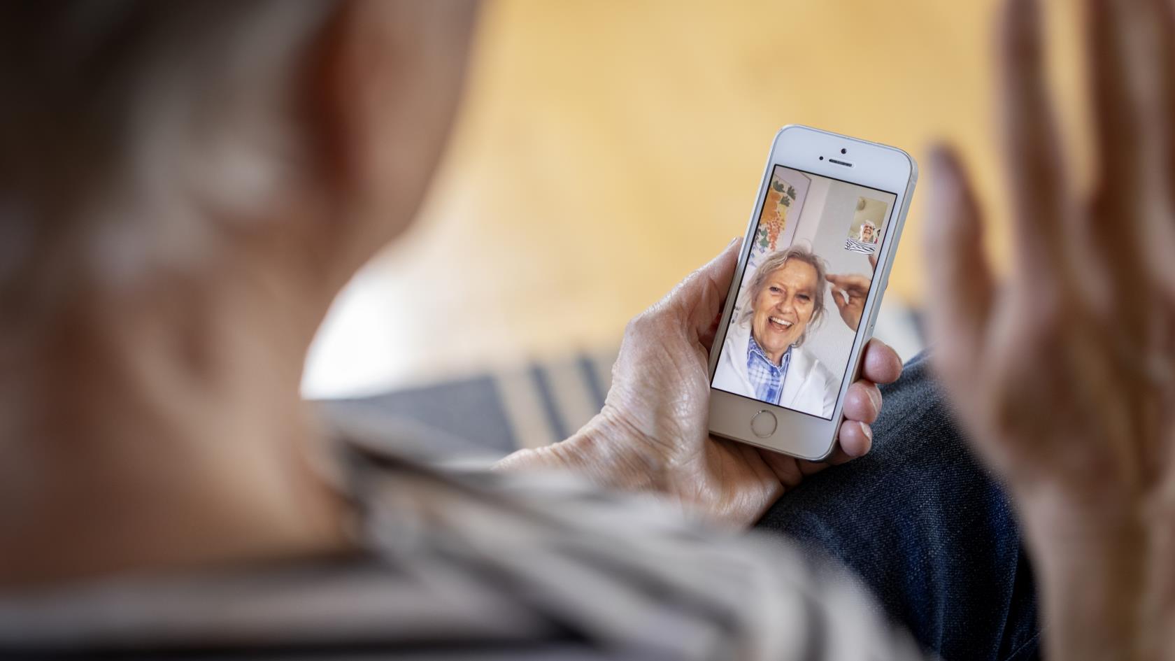 En äldre person har ett videosamtal i mobiltelefonen med en glad äldre kvinna.