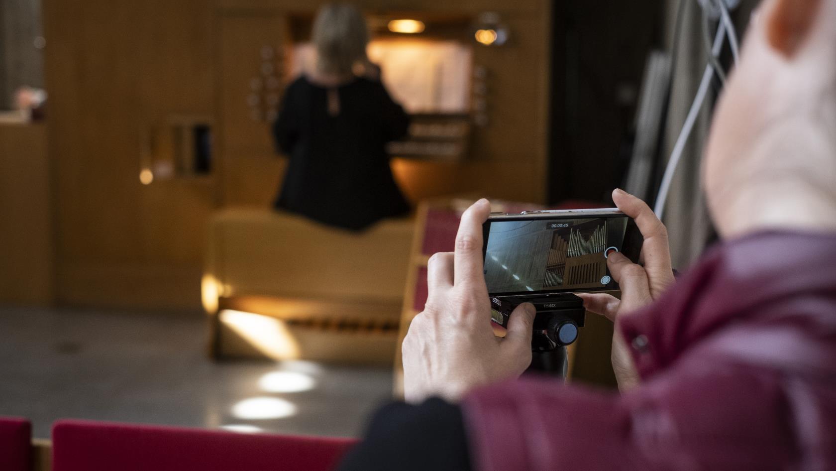 Någon filmar med mobiltelefonen en kvinna som spelar orgel.