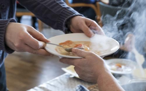 En person serverar soppa och bröd till äldre.