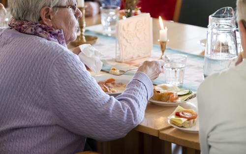 En äldre kvinna sitter och äter tillsammans med andra.