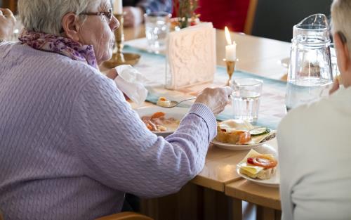 En äldre kvinna sitter och äter tillsammans med andra.