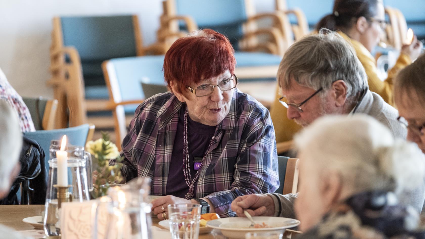 Några äldre personer sitter vid ett bord och äter soppa och samtalar.