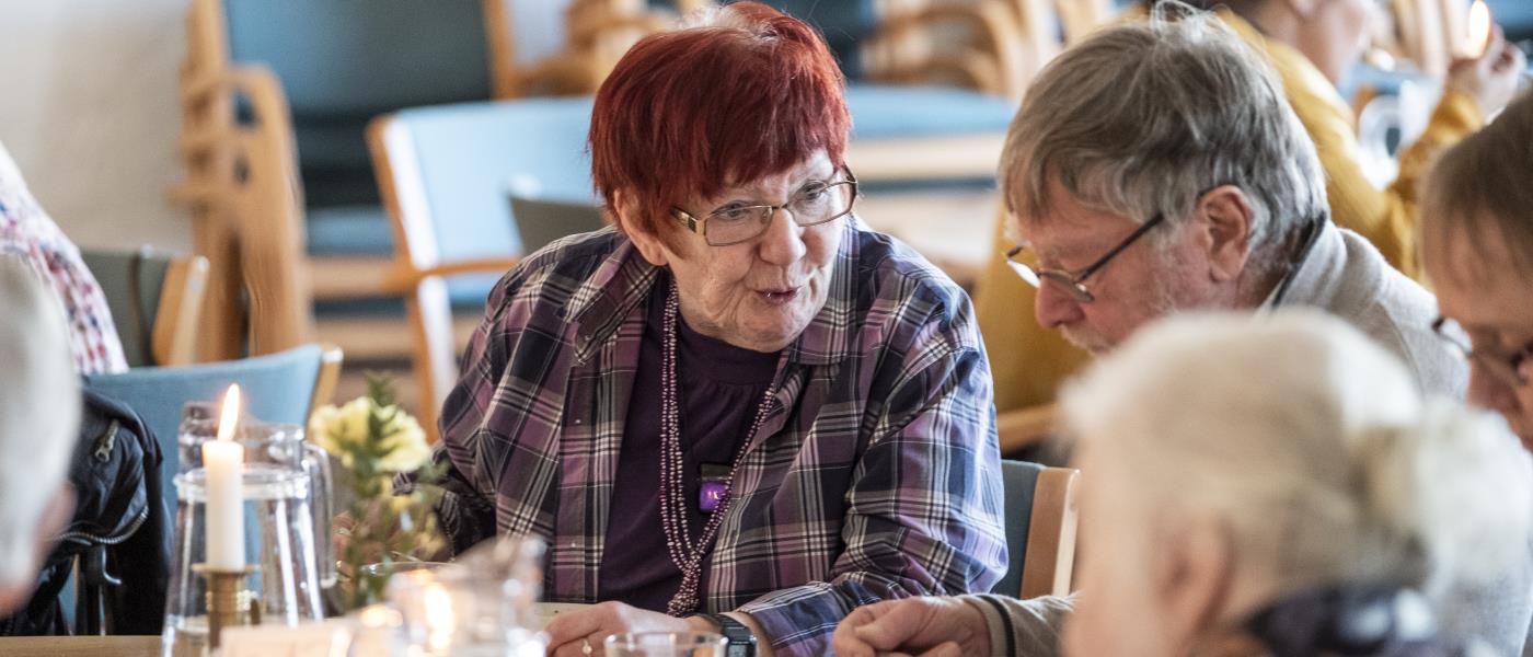 Några äldre personer sitter vid ett bord och äter soppa och samtalar.