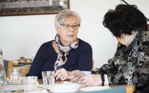 Två äldre damer samtalar vid matbordet.
