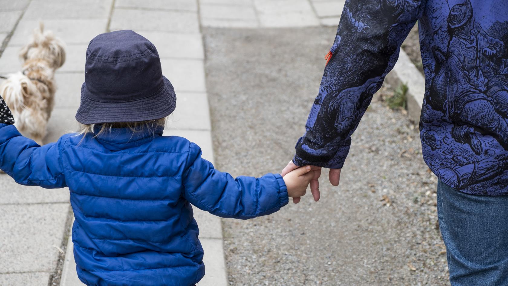 Ett barn håller en vuxen i handen. 