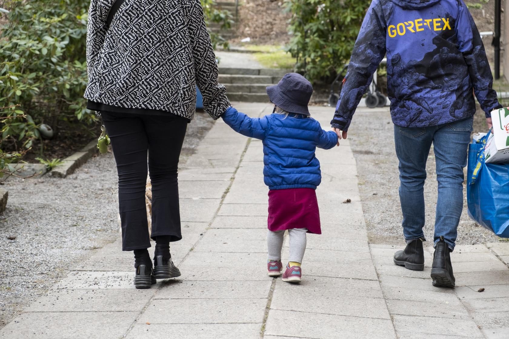 Ett litet barn håller två vuxna i handen på promenaden.