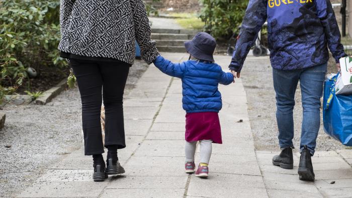 Ett litet barn håller två vuxna i handen på promenaden.