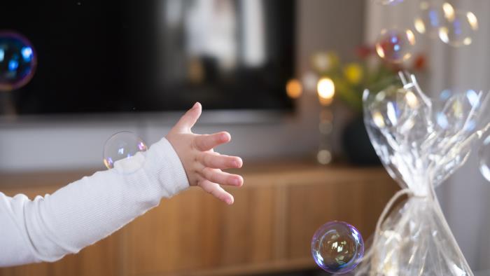 Ett litet barn leker med såpbubblor inomhus.