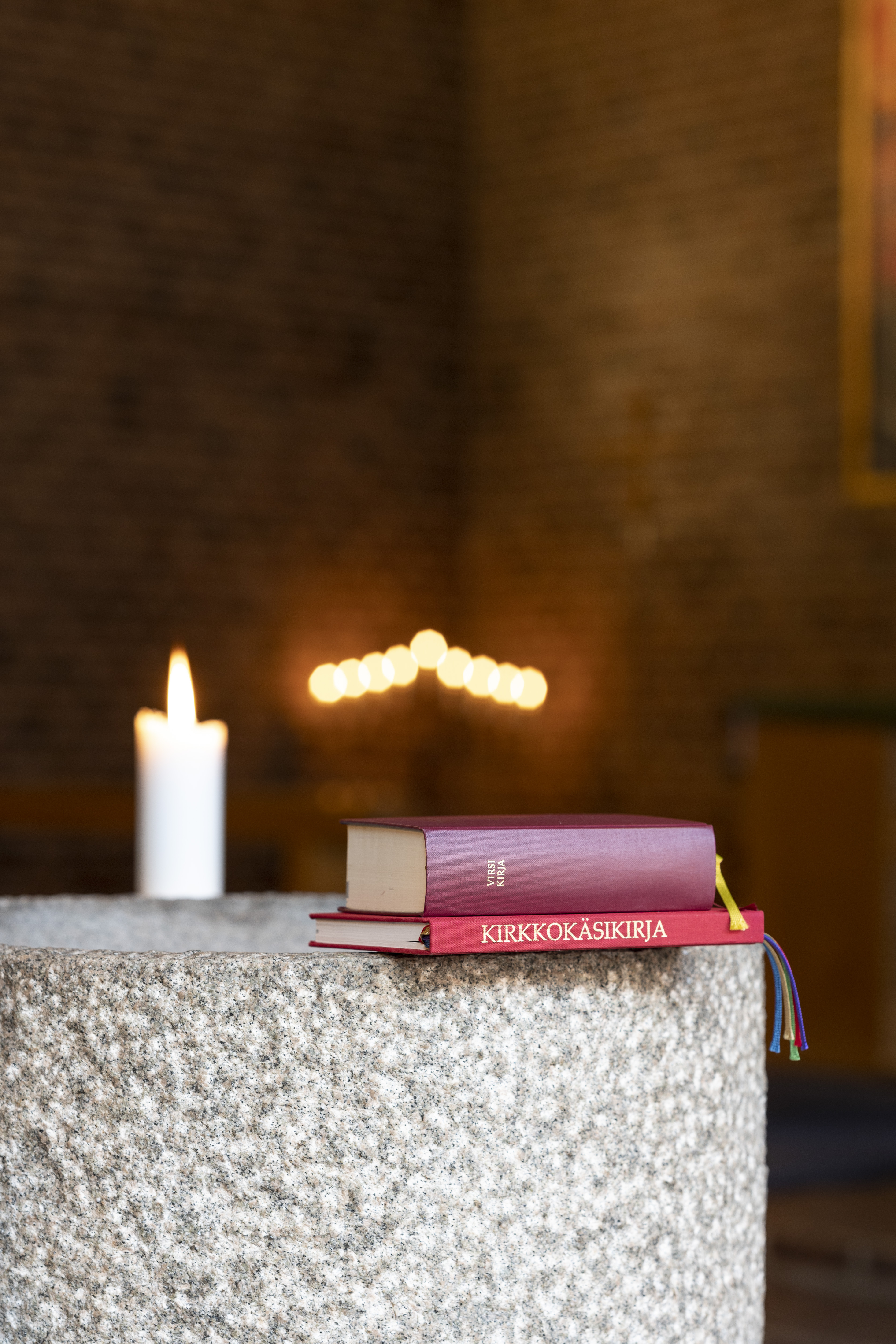 En finsk kyrkohandbok och en psalmbok ligger på kanten av en dopfunt.